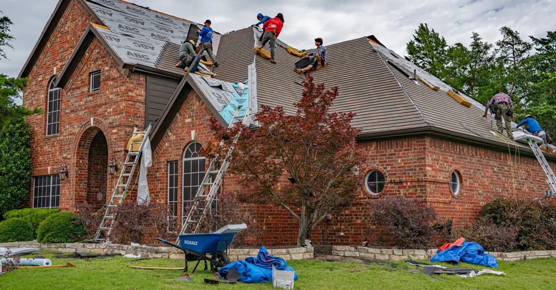 Roofers working on brick home, addressing shingles and roofing materials.